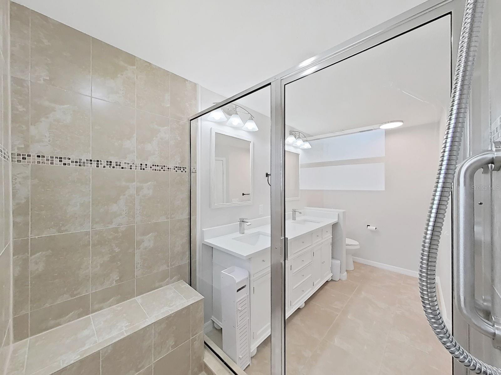 Primary En-suite bathroom.  Spacious shower has a nicely sized bench and stylish tile.  Vanity is new with double sinks. Linen closet and new toilet top it off!