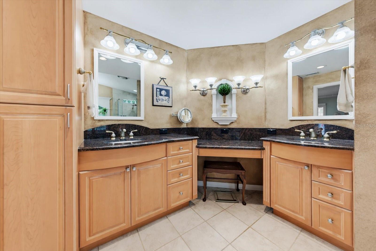 Primary bathroom with double vanities, wood cabinets, granite counters