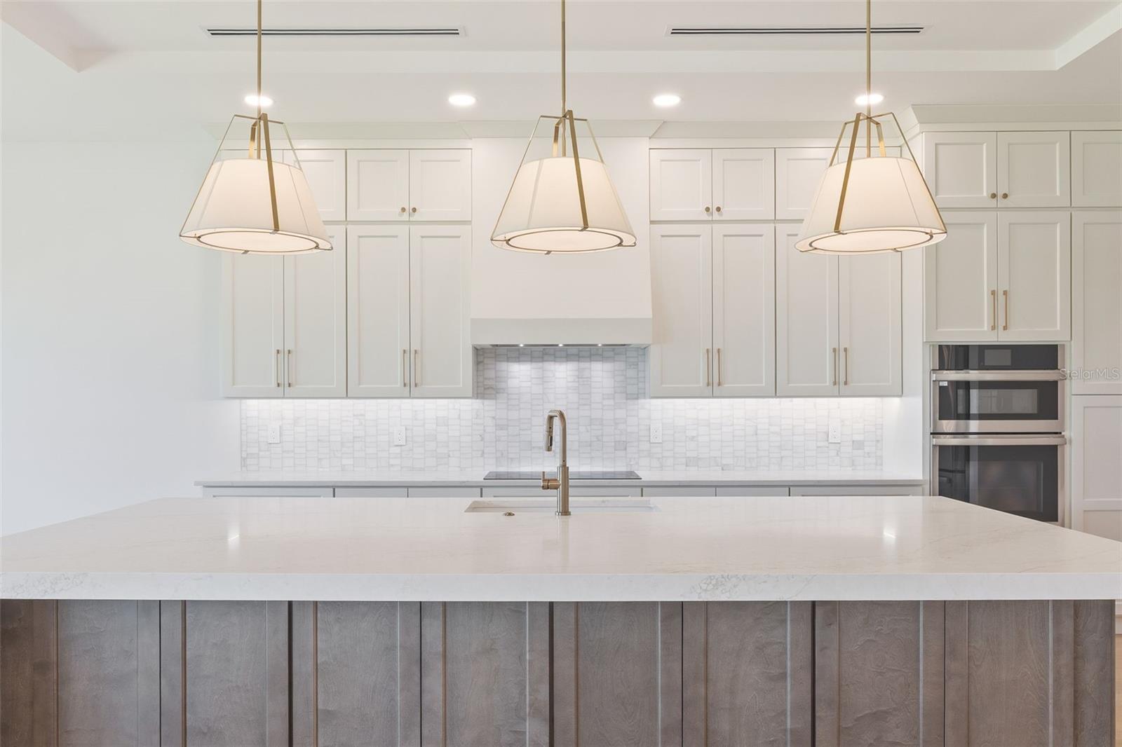 The gourmet kitchen is a true showpiece, featuring full-height custom cabinetry, an oversized 11-foot quartz island with storage on both sides, marble backsplash, GE Profile appliances, custom range hood, cooktop, wall oven, and soft-close cabinetry throughout.
