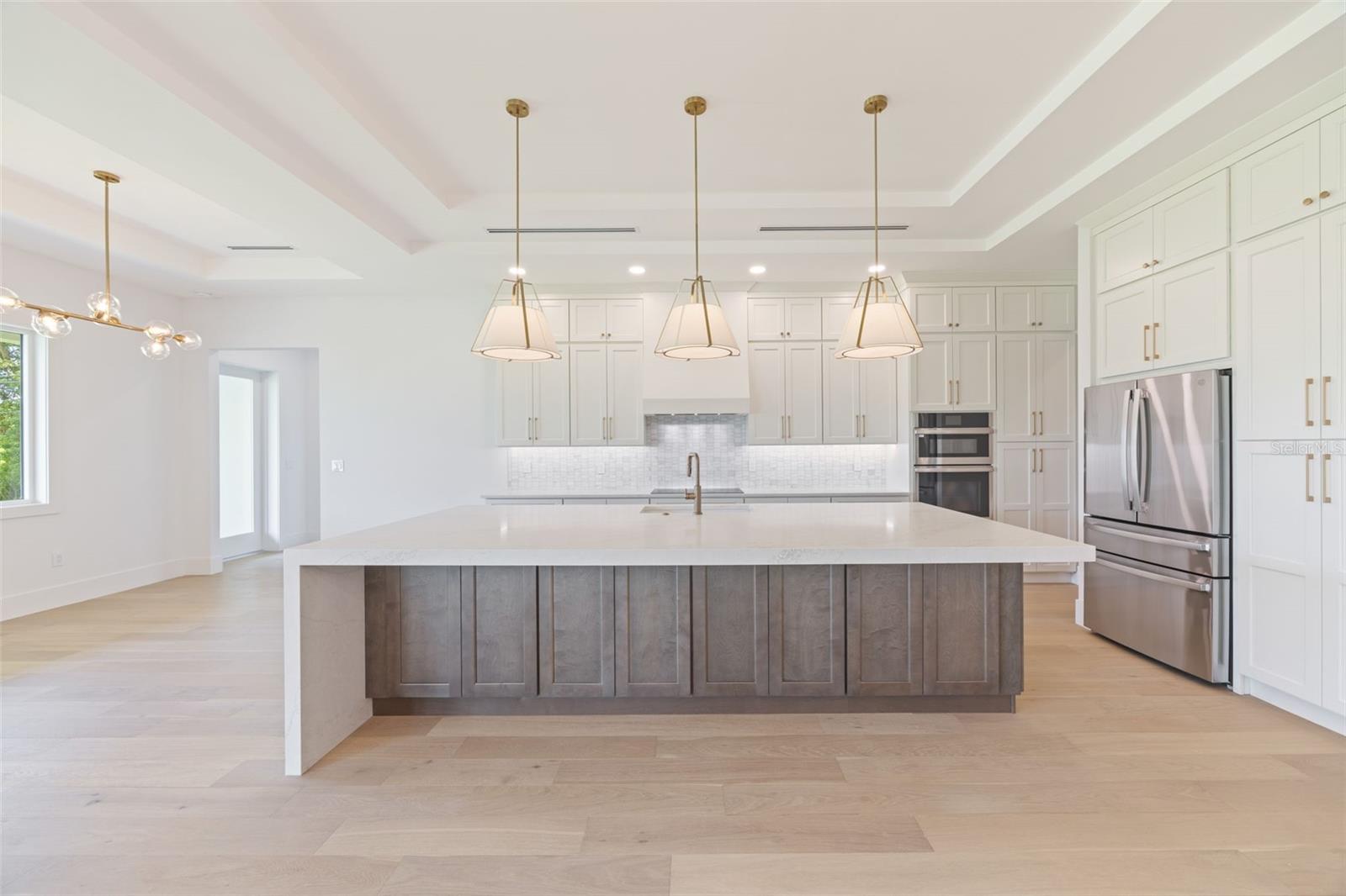 The gourmet kitchen is a true showpiece, featuring full-height custom cabinetry, an oversized 11-foot quartz island with storage on both sides, marble backsplash, GE Profile appliances, custom range hood, cooktop, wall oven, and soft-close cabinetry throughout.