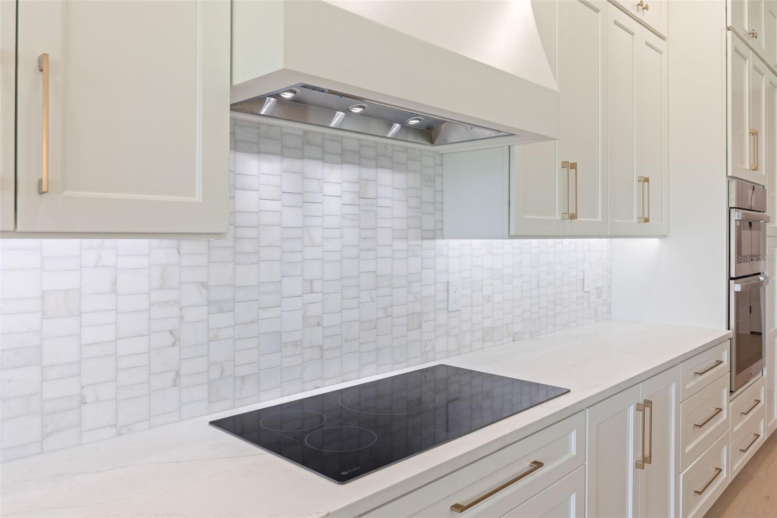 The gourmet kitchen is a true showpiece, featuring full-height custom cabinetry, an oversized 11-foot quartz island with storage on both sides, marble backsplash, GE Profile appliances, custom range hood, cooktop, wall oven, and soft-close cabinetry throughout.