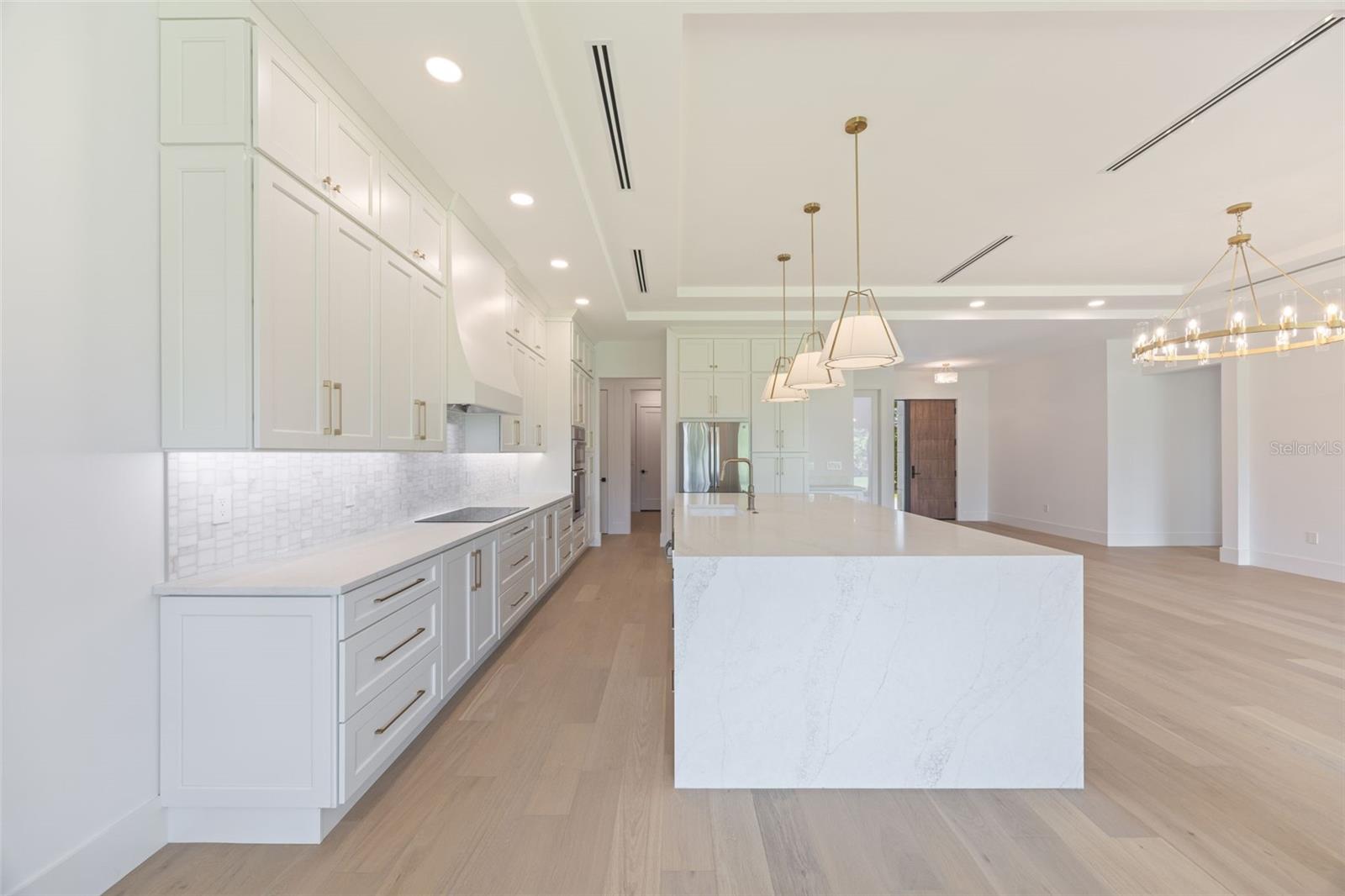 The gourmet kitchen is a true showpiece, featuring full-height custom cabinetry, an oversized 11-foot quartz island with storage on both sides, marble backsplash, GE Profile appliances, custom range hood, cooktop, wall oven, and soft-close cabinetry throughout.