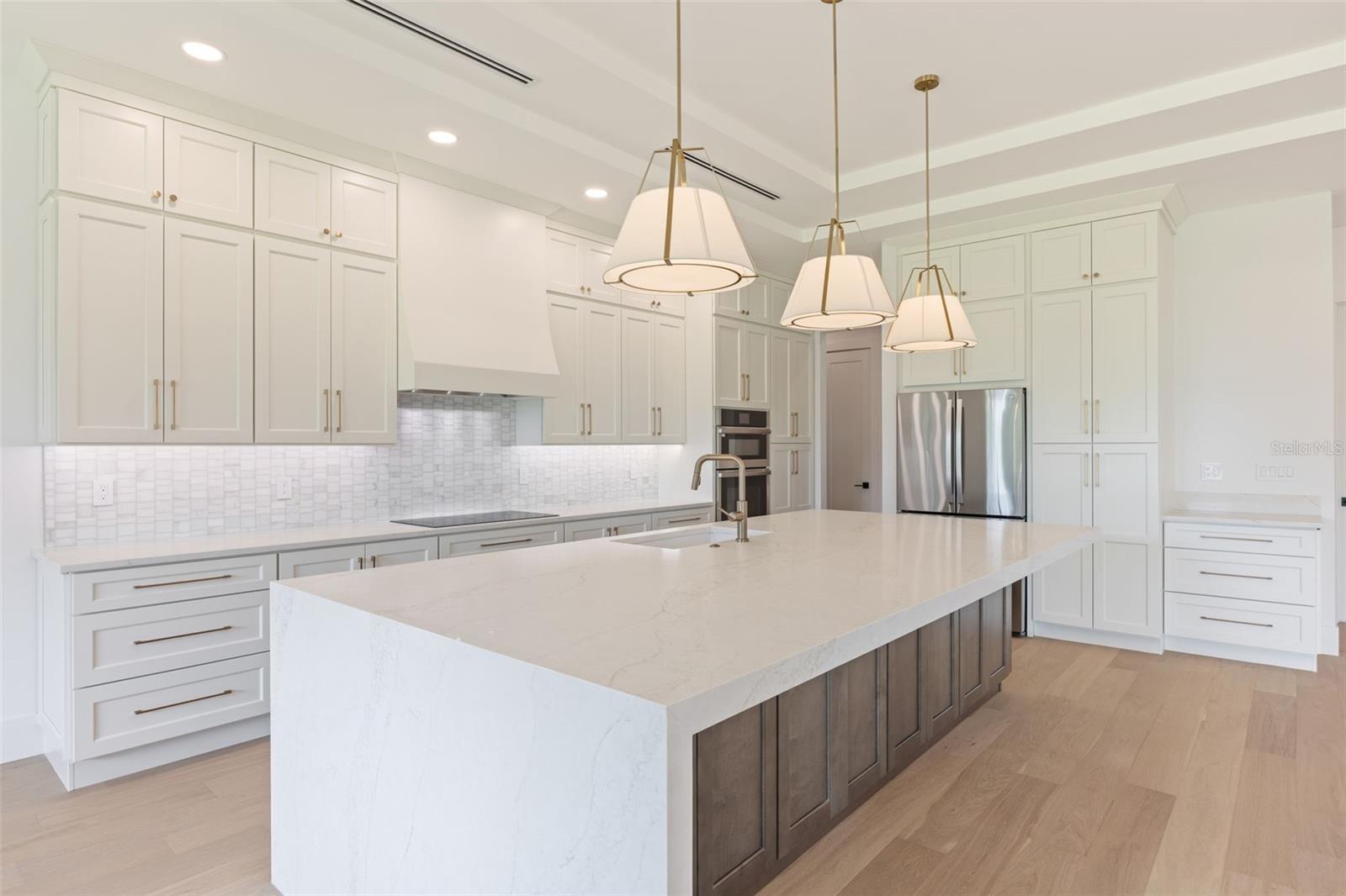 The gourmet kitchen is a true showpiece, featuring full-height custom cabinetry, an oversized 11-foot quartz island with storage on both sides, marble backsplash, GE Profile appliances, custom range hood, cooktop, wall oven, and soft-close cabinetry throughout.