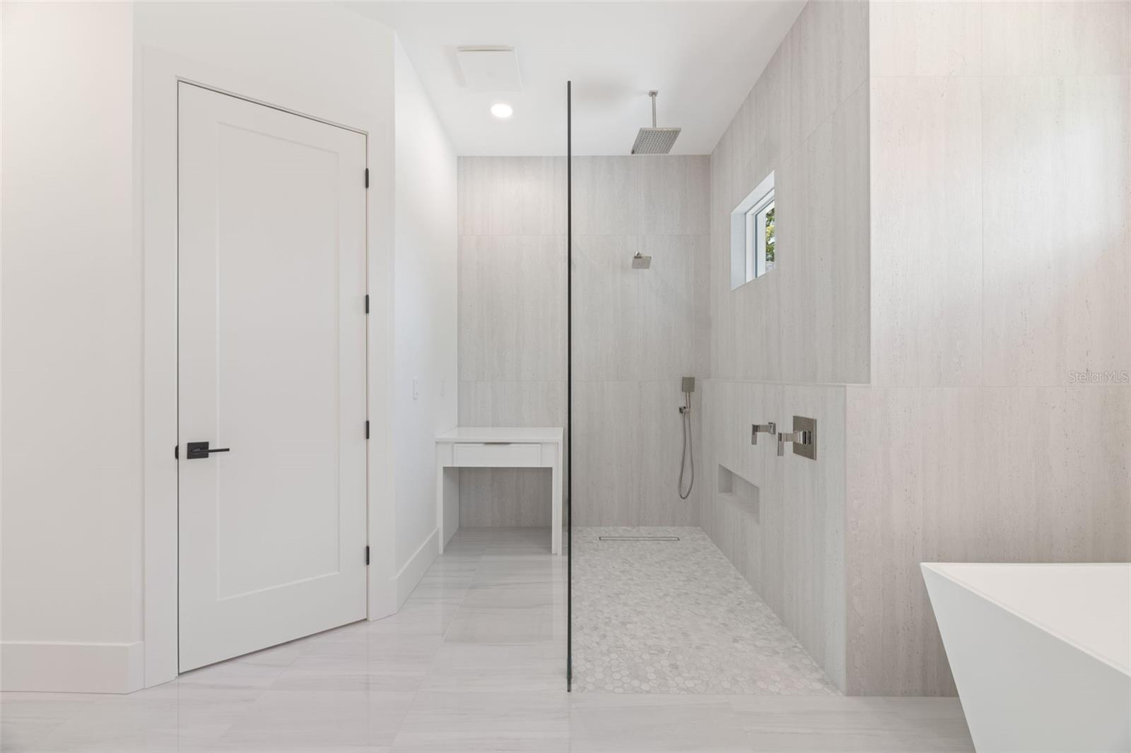The luxurious primary suite offers a spa-inspired retreat featuring a freestanding soaking tub, oversized walk-in shower with rain head and handheld shower, premium Italian tile, designer fixtures, and thoughtful custom details throughout.