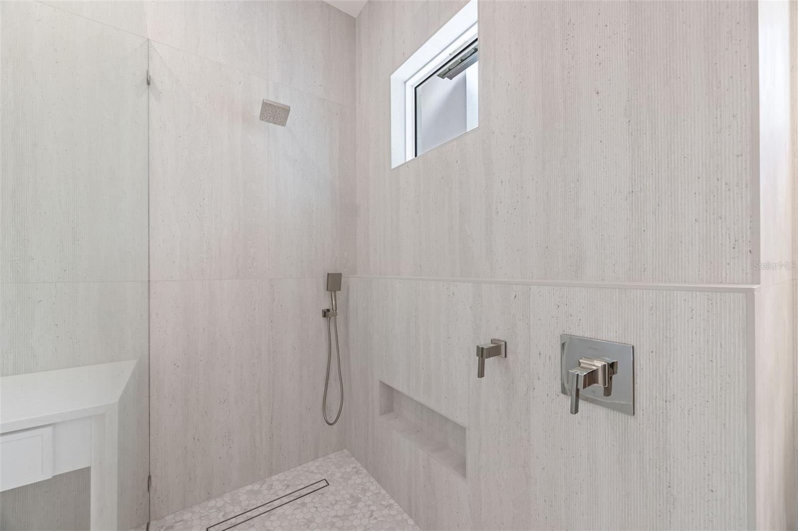 The luxurious primary suite offers a spa-inspired retreat featuring a freestanding soaking tub, oversized walk-in shower with rain head and handheld shower, premium Italian tile, designer fixtures, and thoughtful custom details throughout.
