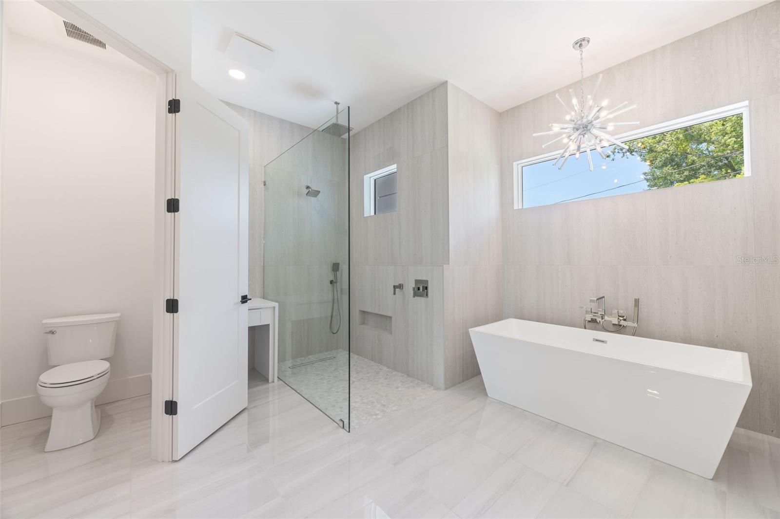 The luxurious primary suite offers a spa-inspired retreat featuring a freestanding soaking tub, oversized walk-in shower with rain head and handheld shower, premium Italian tile, designer fixtures, and thoughtful custom details throughout.