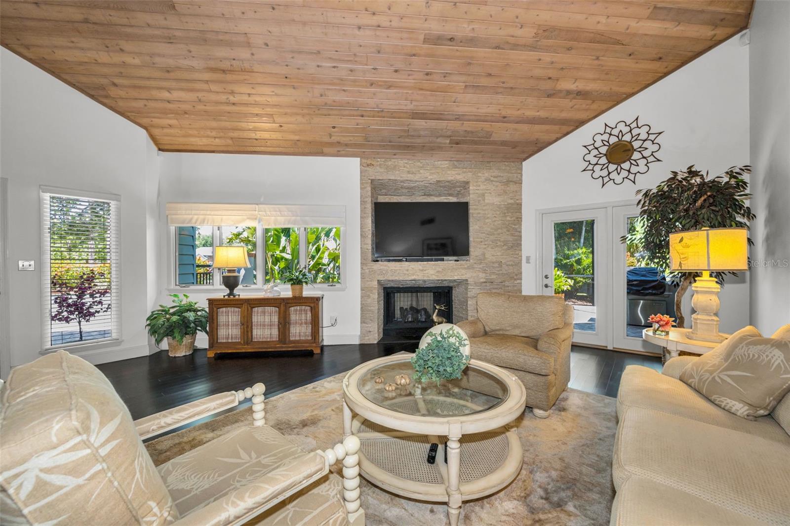 Living room with gas fireplace and tongue and groove volume ceiling! The french doors lead to the screened outdoor patio and grill area overlooking the serene pond.