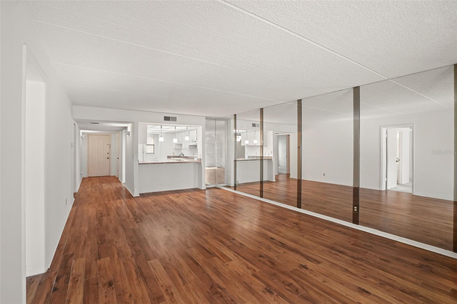 Spacious from Every Angle. The open living and dining areas are anchored by warm laminate flooring, a breakfast bar with pendant lighting, and a mirrored wall that enhances the room.