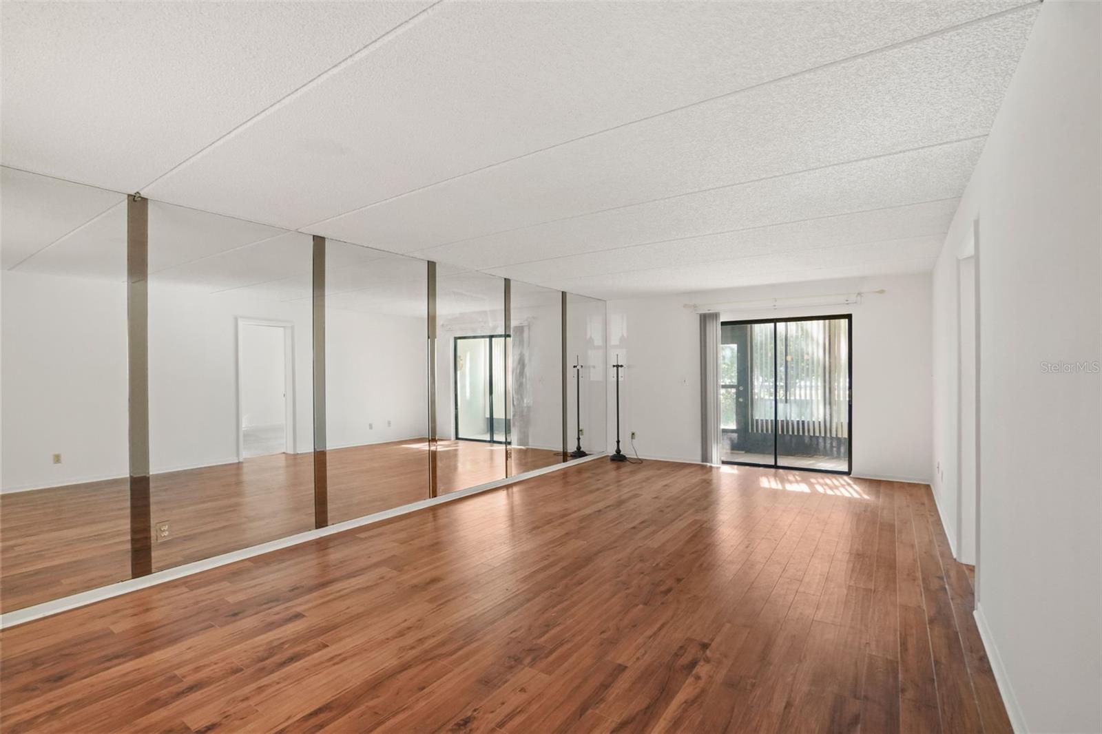 Designed to Feel Open. Continuous laminate flooring, a mirrored accent wall, and sliding glass doors to the screened lanai create an airy, inviting main living space.