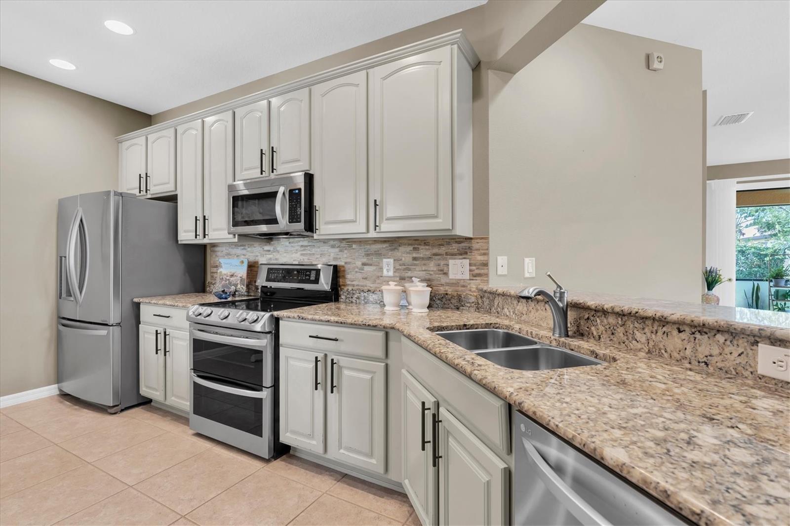 Updated kitchen with glass tile backsplash, granite counters, light modern  cabinets and hardware, new stainless appliances.