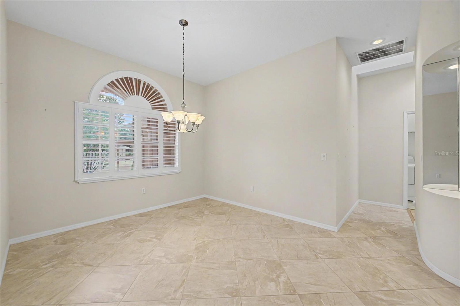 Formal dining room, highlighting its neutral color palette and spacious layout. The room features plantation shutters, abundant natural light, and detailed baseboards, showcasing the quality finishes and versatile use of the space.