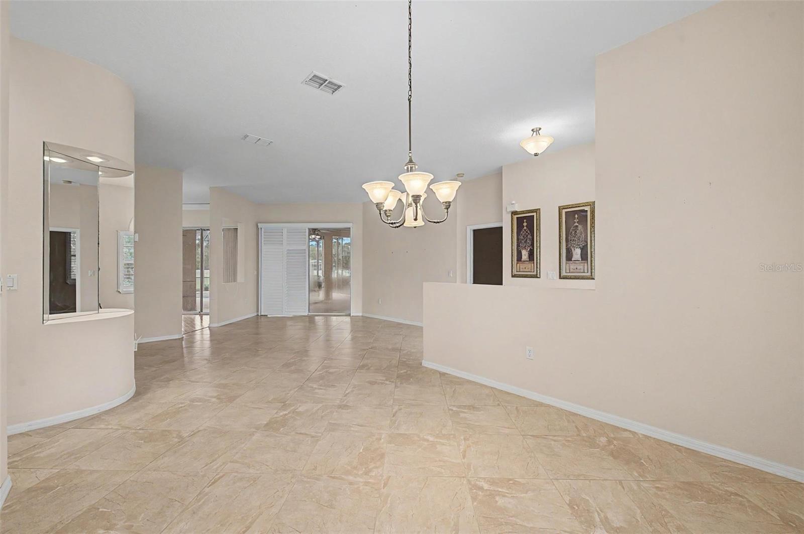 Dining area with a clear view into the formal sitting room, showcasing an open and connected floor plan. The space features a sliding glass door with plantation shutters, providing direct access to the pool area and bringing in abundant natural light. Neutral tones and quality finishes enhance the home’s seamless indoor-outdoor living experience.