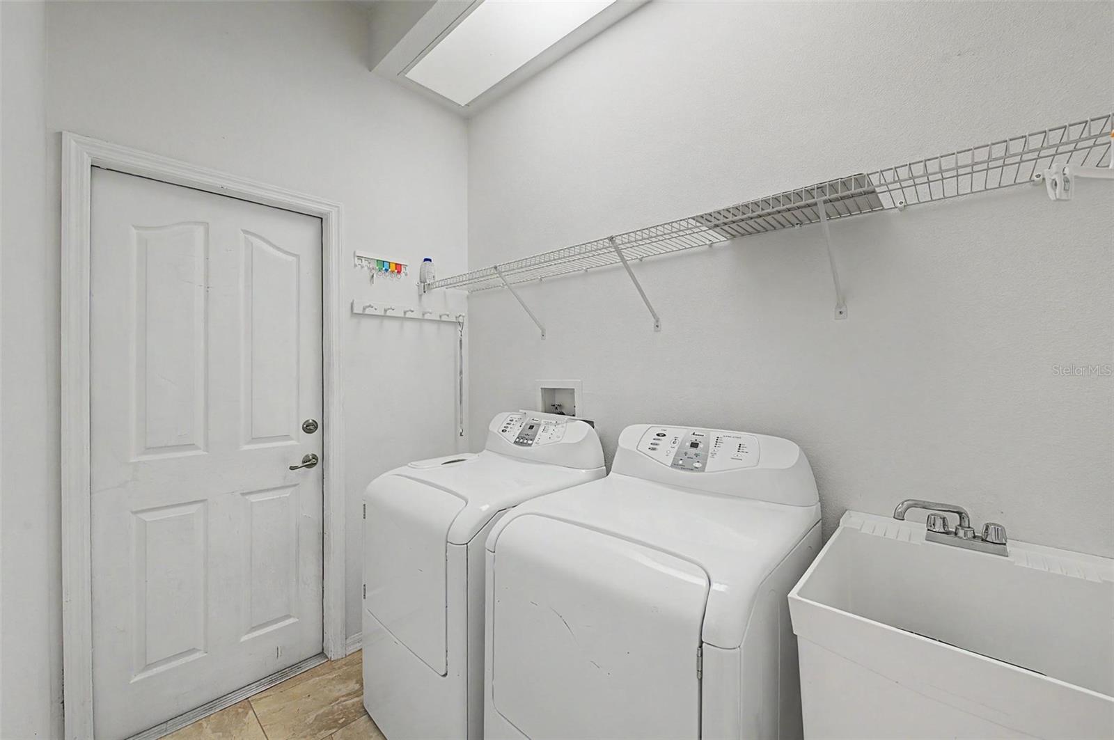 Fully functional laundry room equipped with a washer and dryer, both included with the home. The space also features a utility sink, overhead hanging rack for air-drying garments, and ample room for everyday laundry tasks, combining convenience with practical functionality.