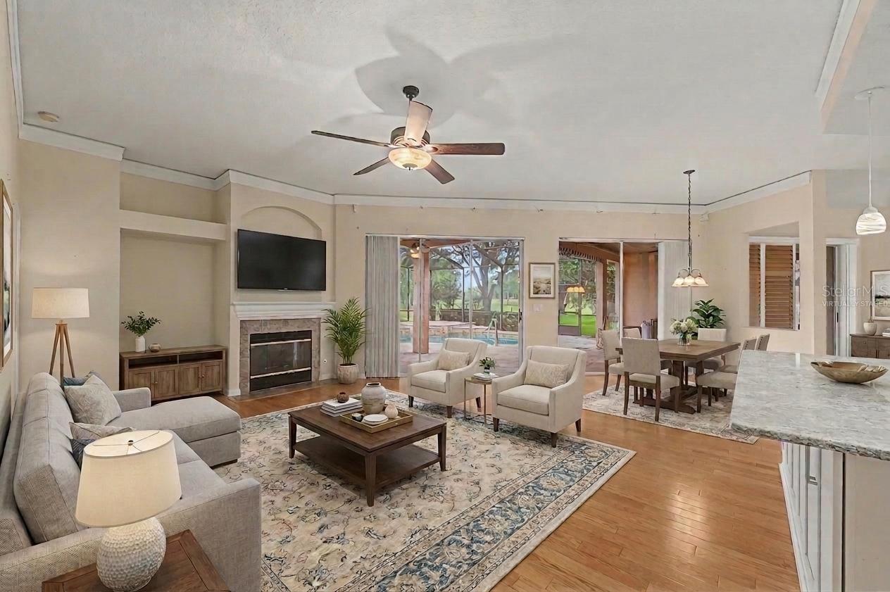 Main living room featuring a spacious, virtually staged layout with flexible areas for both seating and dining. The room showcases wood plank flooring, detailed baseboards, and a fireplace as a focal point. Two large sliding glass doors provide abundant natural light and open to views of the pool and a nearby golf course hole, enhancing the indoor-outdoor living experience.