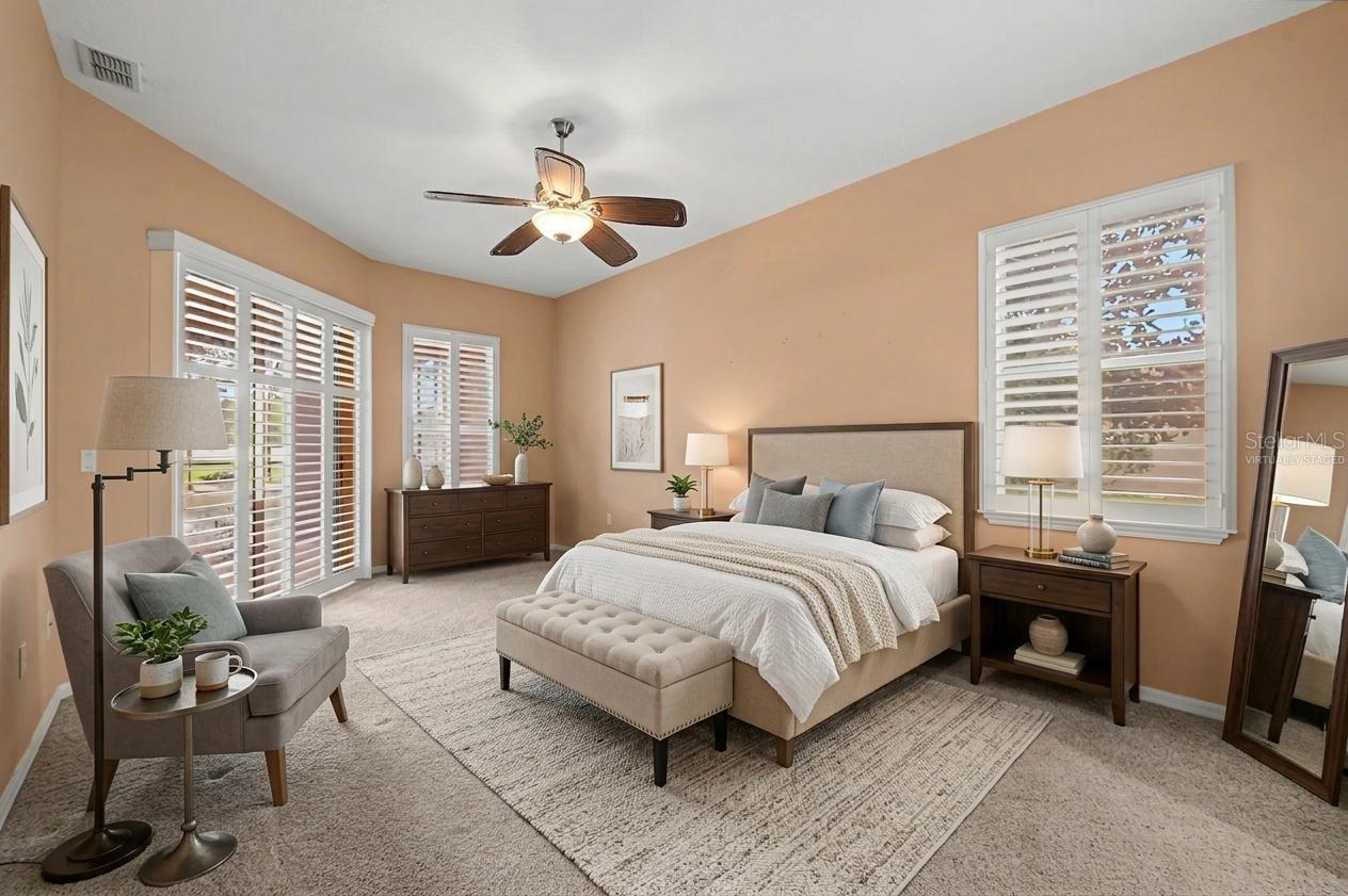 Spacious master suite featuring abundant natural light and a well-designed layout with space for a sitting area. The bedroom offers direct access to the outdoor pool area through sliding glass doors, creating seamless indoor-outdoor living. Large windows are fitted with plantation shutters for privacy and light control, while the virtually staged design highlights the room’s generous scale and comfort.