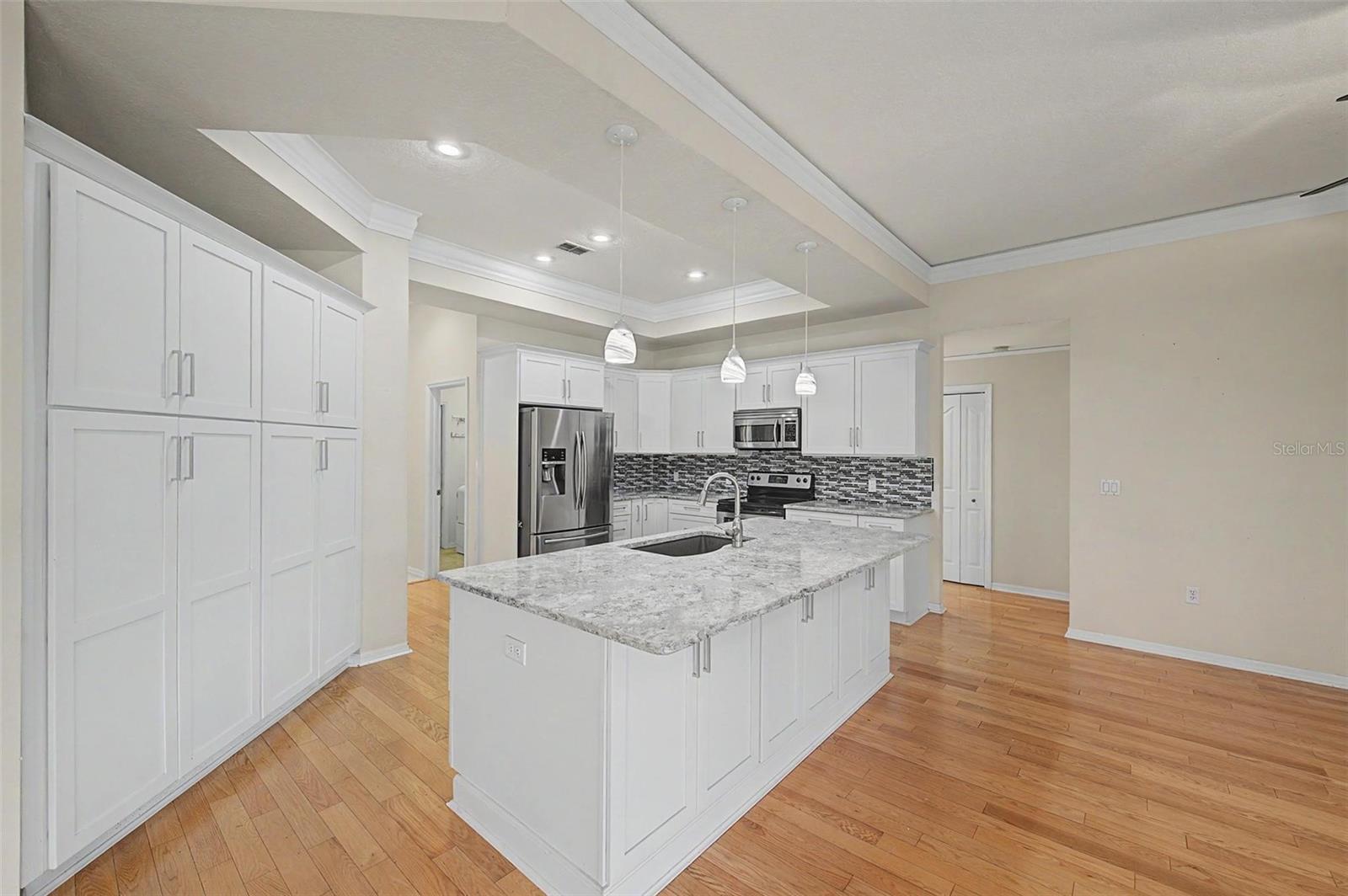 The oversized granite island serves as the heart of the kitchen, featuring built-in electrical outlets for convenient use of small appliances and device charging. Thoughtfully designed with cabinetry on both the working side and the seating side, the island provides exceptional storage while offering ample space for casual dining and entertaining. Complete with abundant cabinetry, a stylish tile backsplash, stainless steel appliances, recessed and pendant lighting, and generous counter space, this kitchen is as functional as it is beautiful.