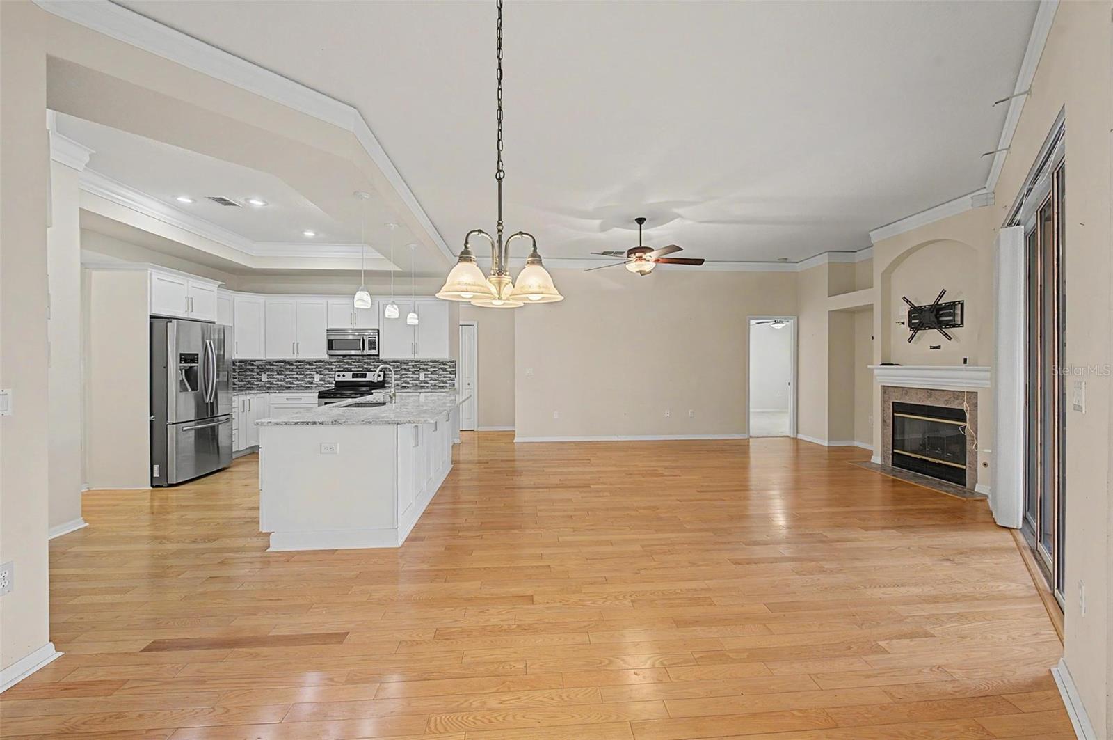 Expansive open-concept view showcasing the seamless flow between the main living room, dining area, and kitchen. Thoughtfully designed for both everyday living and entertaining, the space features abundant natural light, wood-look flooring, and an inviting layout that connects each living area while maintaining a warm and spacious feel.