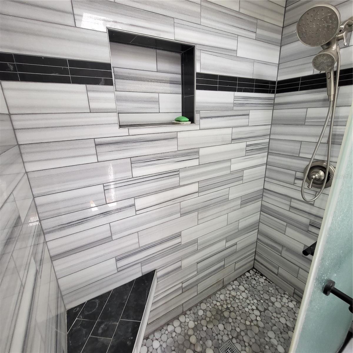 Beautifully tiled shower features bench, built in product shelf and a dual shower head.