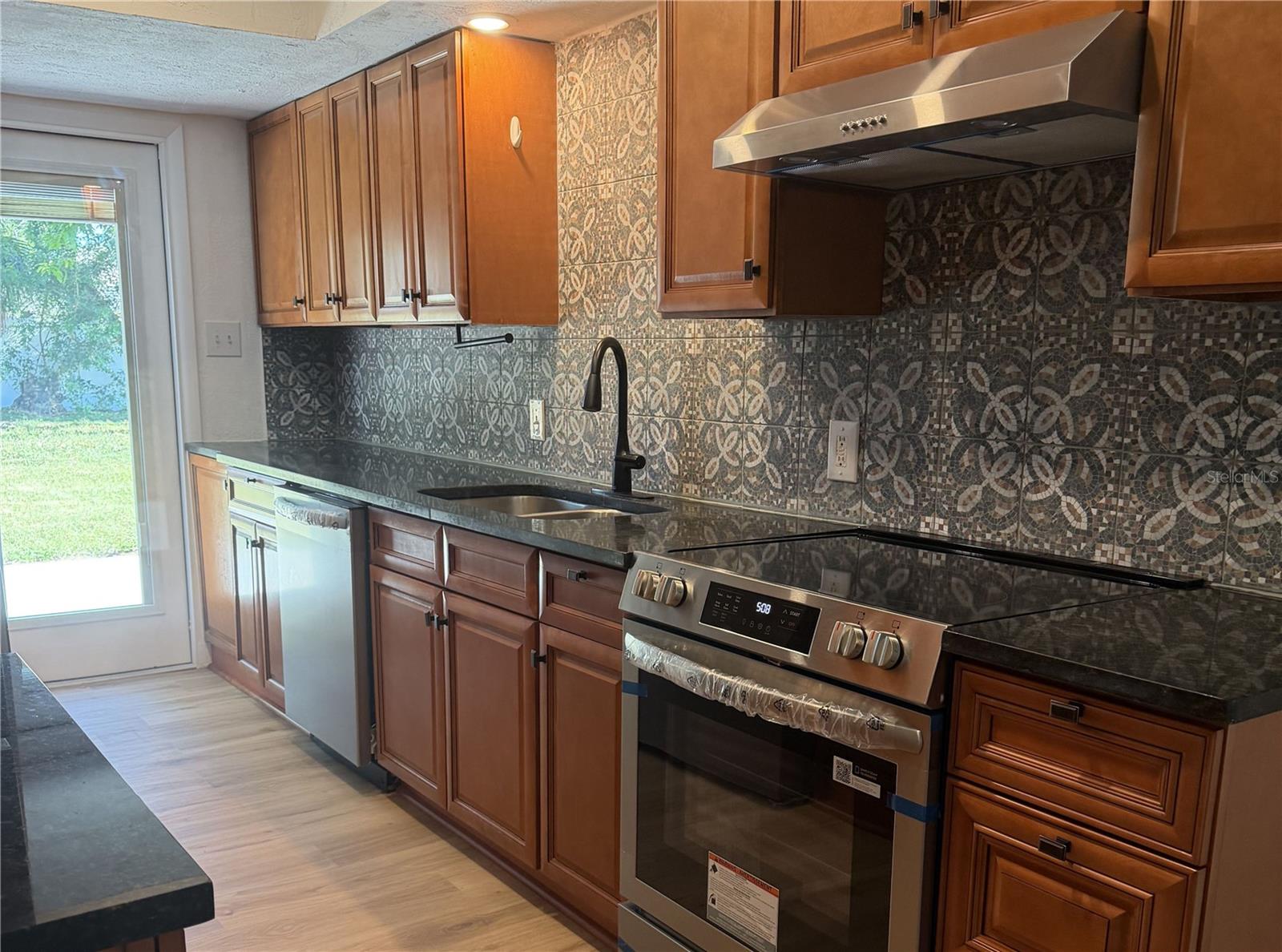 A Cook's Delight - Stunning warm cabinetry and sleek, dark granite countertops. Beautifully accented by a detailed, full-height mosaic tile backsplash adding incredible texture and modern flair. High-end stainless steel appliances complete this chef ready space.