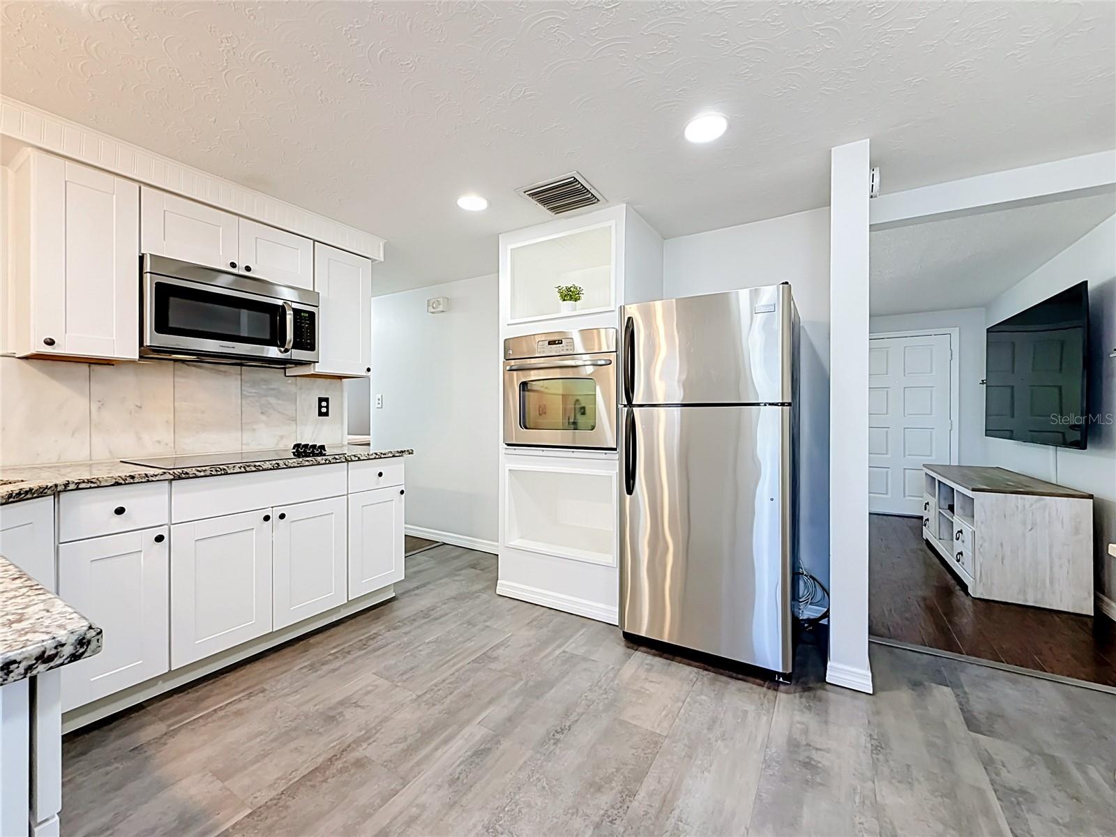 Stylish kitchen with granite countertops, tile backsplash, new luxury laminate flooring, stainless steel appliances, built-in oven, and ample storage