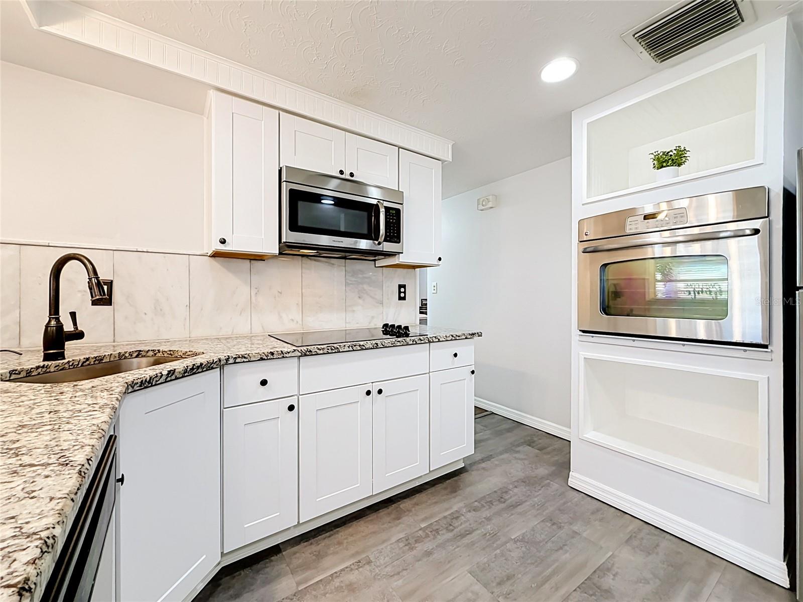 Stylish kitchen with granite countertops, tile backsplash, new luxury laminate flooring, stainless steel appliances, built-in oven, and ample storage
