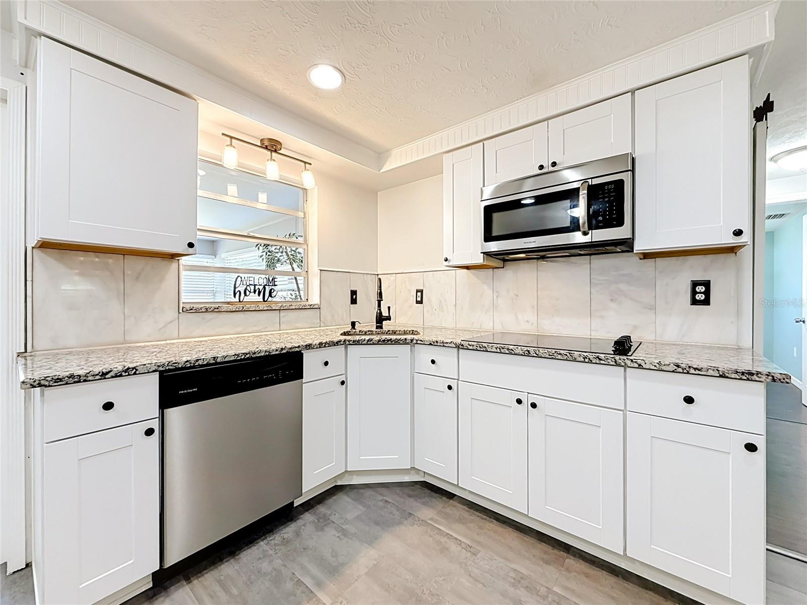 Stylish kitchen with granite countertops, tile backsplash, new luxury laminate flooring, stainless steel appliances, built-in oven, and ample storage