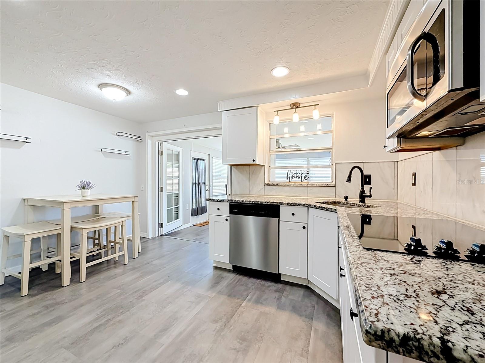 Stylish kitchen with granite countertops, tile backsplash, new luxury laminate flooring, stainless steel appliances, built-in oven, and ample storage