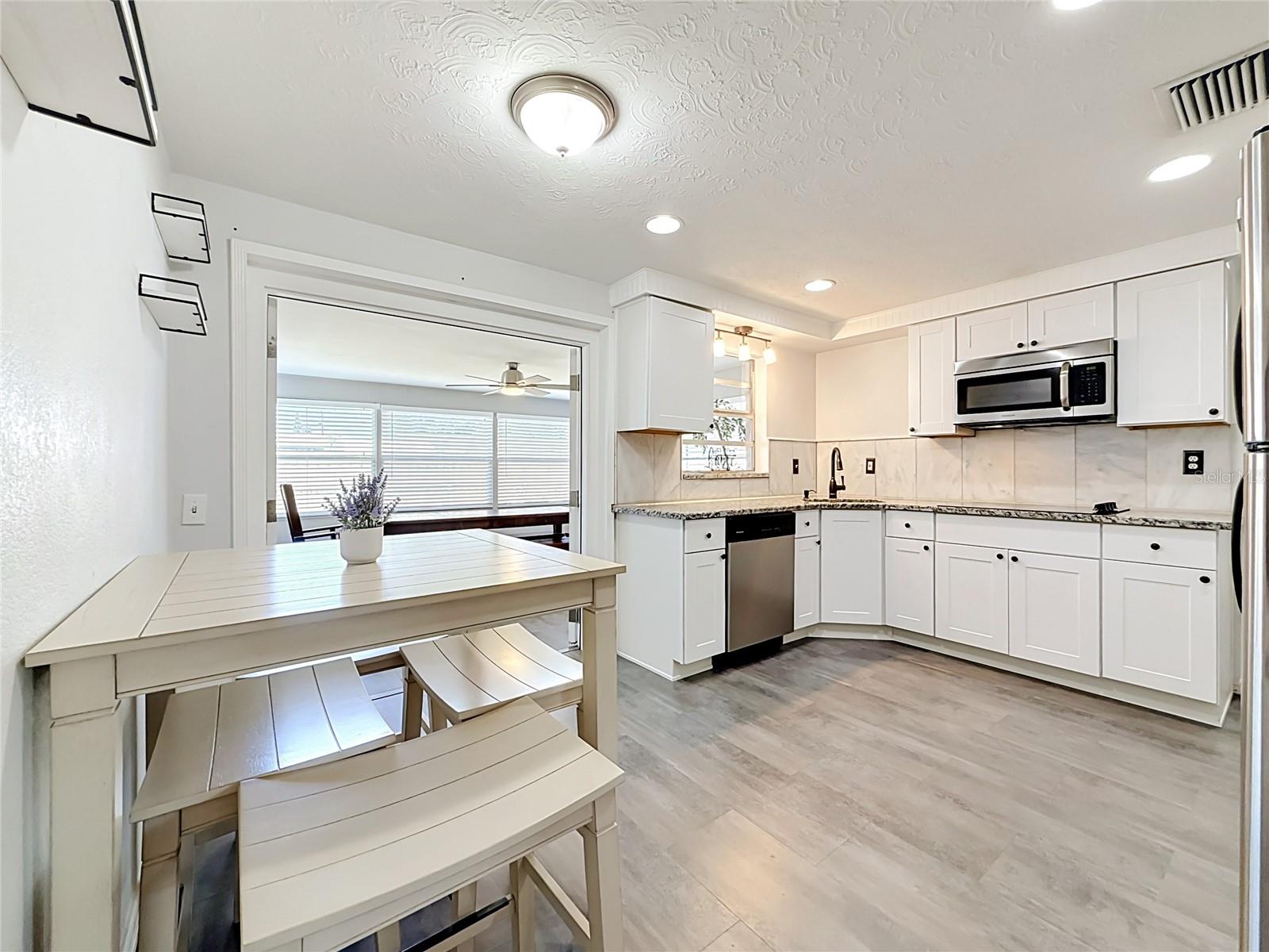 Stylish kitchen with granite countertops, tile backsplash, new luxury laminate flooring, stainless steel appliances, built-in oven, and ample storage