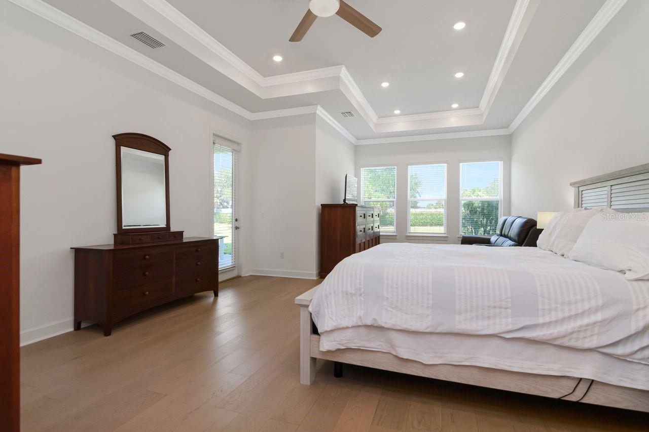 Primary Bedroom with Gorgeous Windows to View Backyard & Water - Tray Ceilings with Crown Molding - Upgraded Ceiling Fan - Door to Access Lanai - Engineered Hardwood Floors