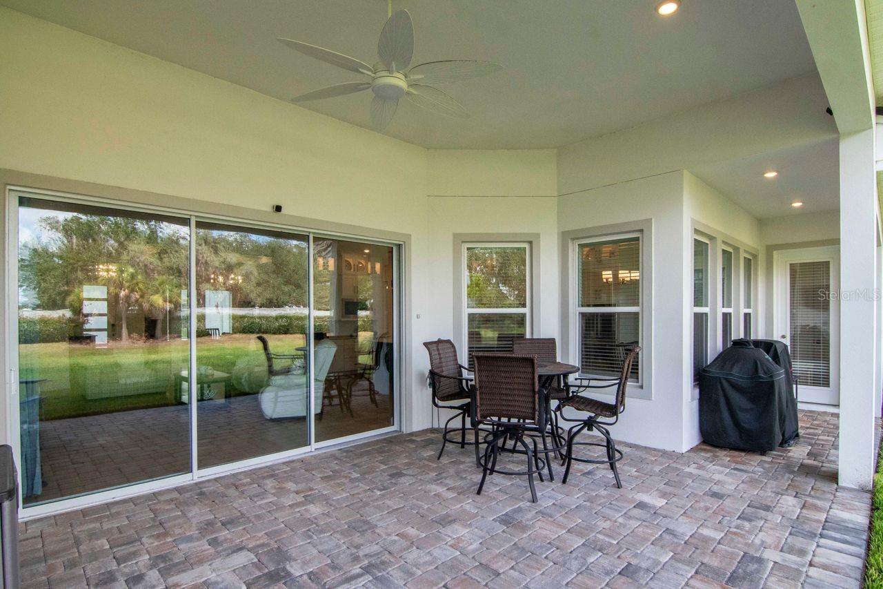Covered Lanai - Triple Sliding Glass Doors Access - Door to Hallway by Full Bathroom - Door to Primary Suite - Paver Floor - Ceiling Fan