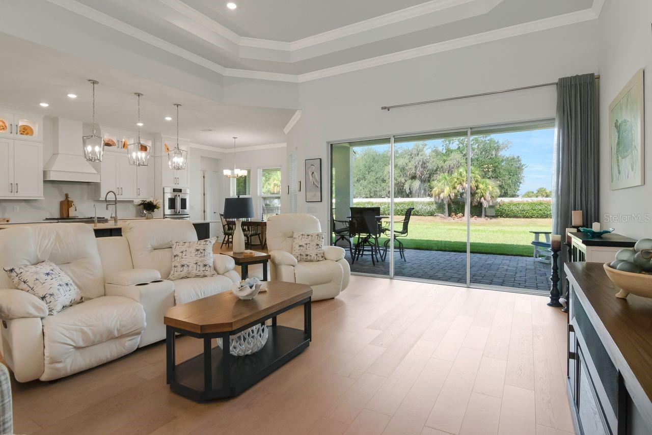 Living Room - Triple Sliding Glass Doors - Tray Ceiling with Crown Molding - Upgraded Ceiling Fan - Engineered Hardwood Floor - Electrical Floor Outlet - View of Kitchen/Eat-In