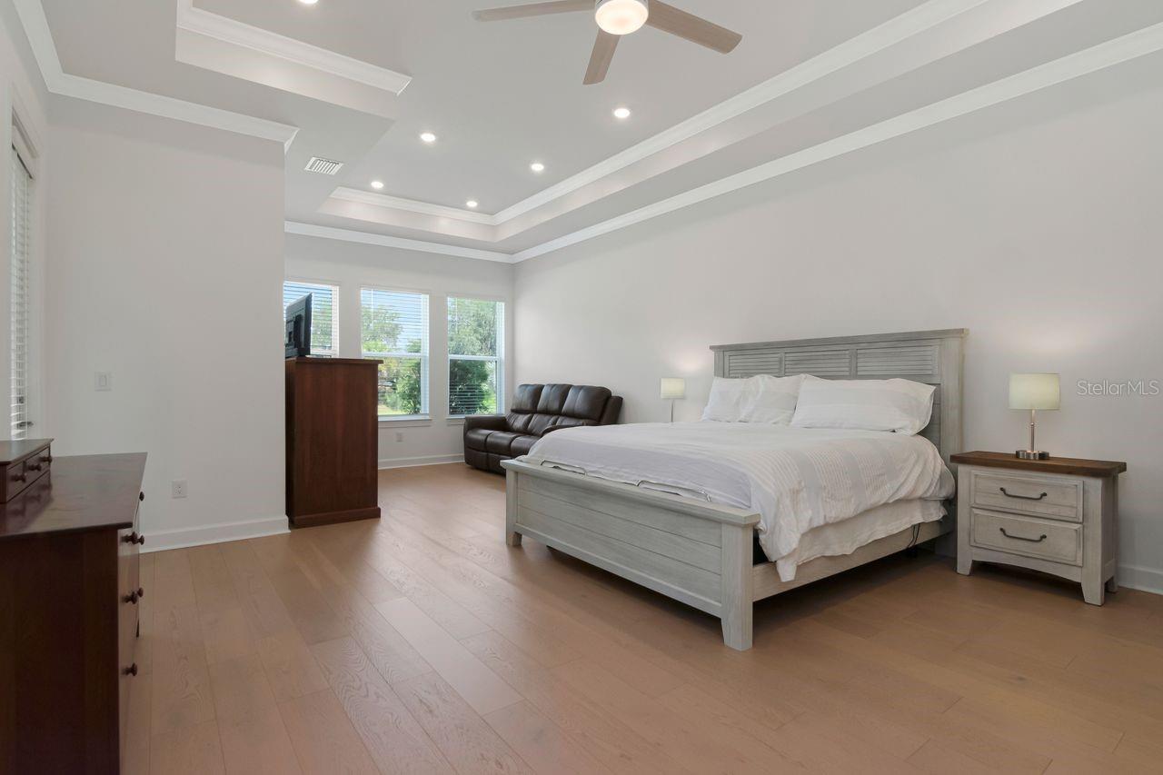 Primary Suite with En-Suite Bathroom - Windows to View of Backyard/Pond - Extended Sitting Room Area - Tray Ceiling with Crown Molding - Engineered Hardwood Floor - Door to Access Lanai - Recessed Lighting