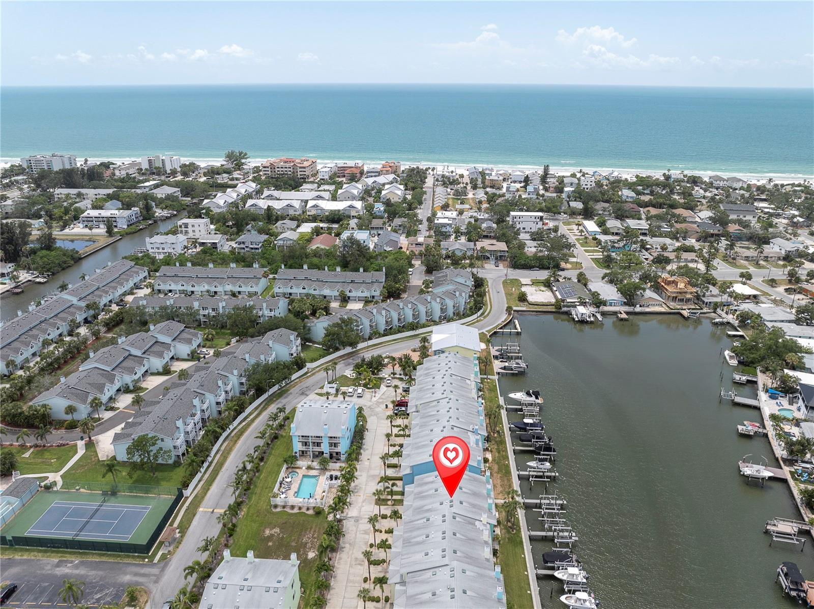 A bird's-eye look at life in Sunset Bay — a row of pastel townhomes tucked along the Intracoastal, docks lined with boats, and the Gulf shimmering in the distance. This is the view that sells the lifestyle before you even step inside.