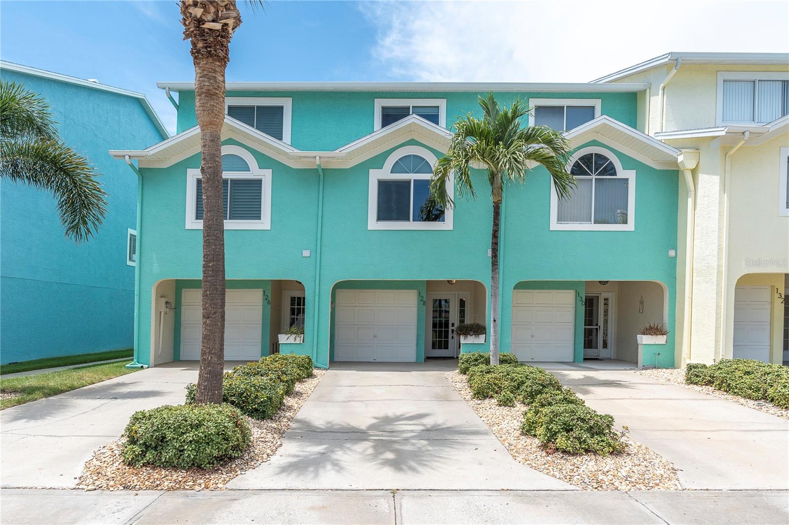 Sun-washed teal and coastal pastels, palm trees framing the entry, a driveway that says "you've arrived." This is the first impression — and it doesn't disappoint.