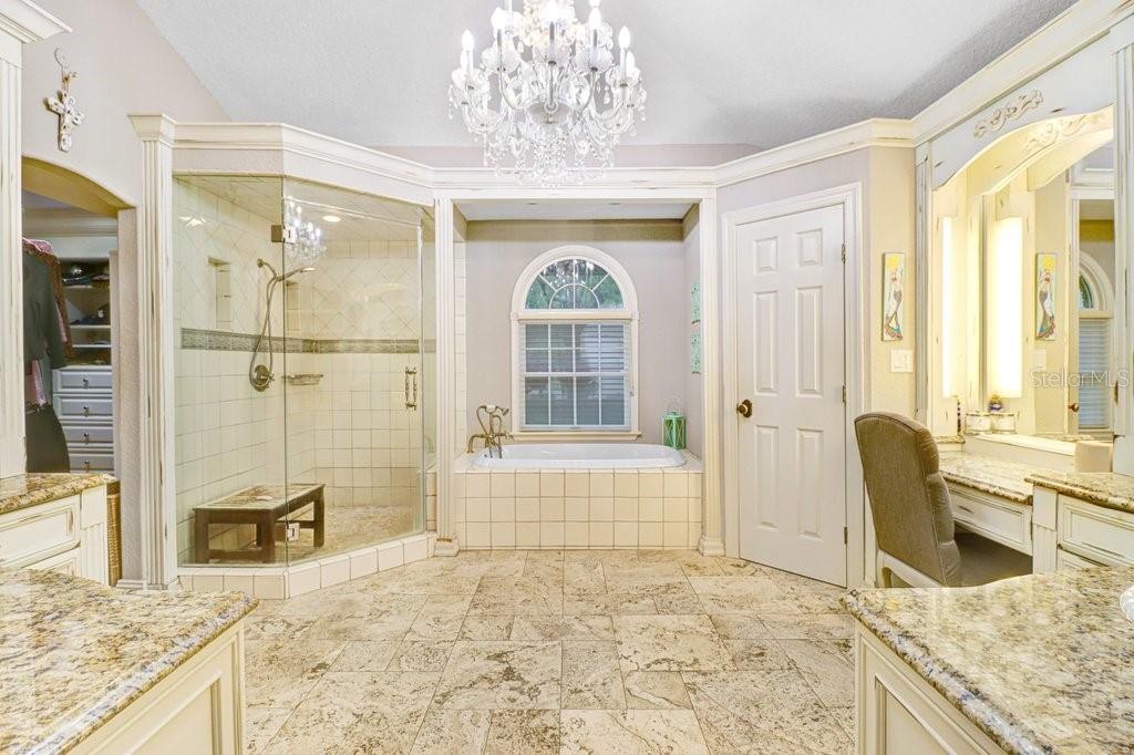 Amazing master bathroom with beautiful custom lighting and chandelier with steam shower, vanity area, large Roman soaking tub, and his and her sink areas that include custom cabinetry and granite counter tops throughout.