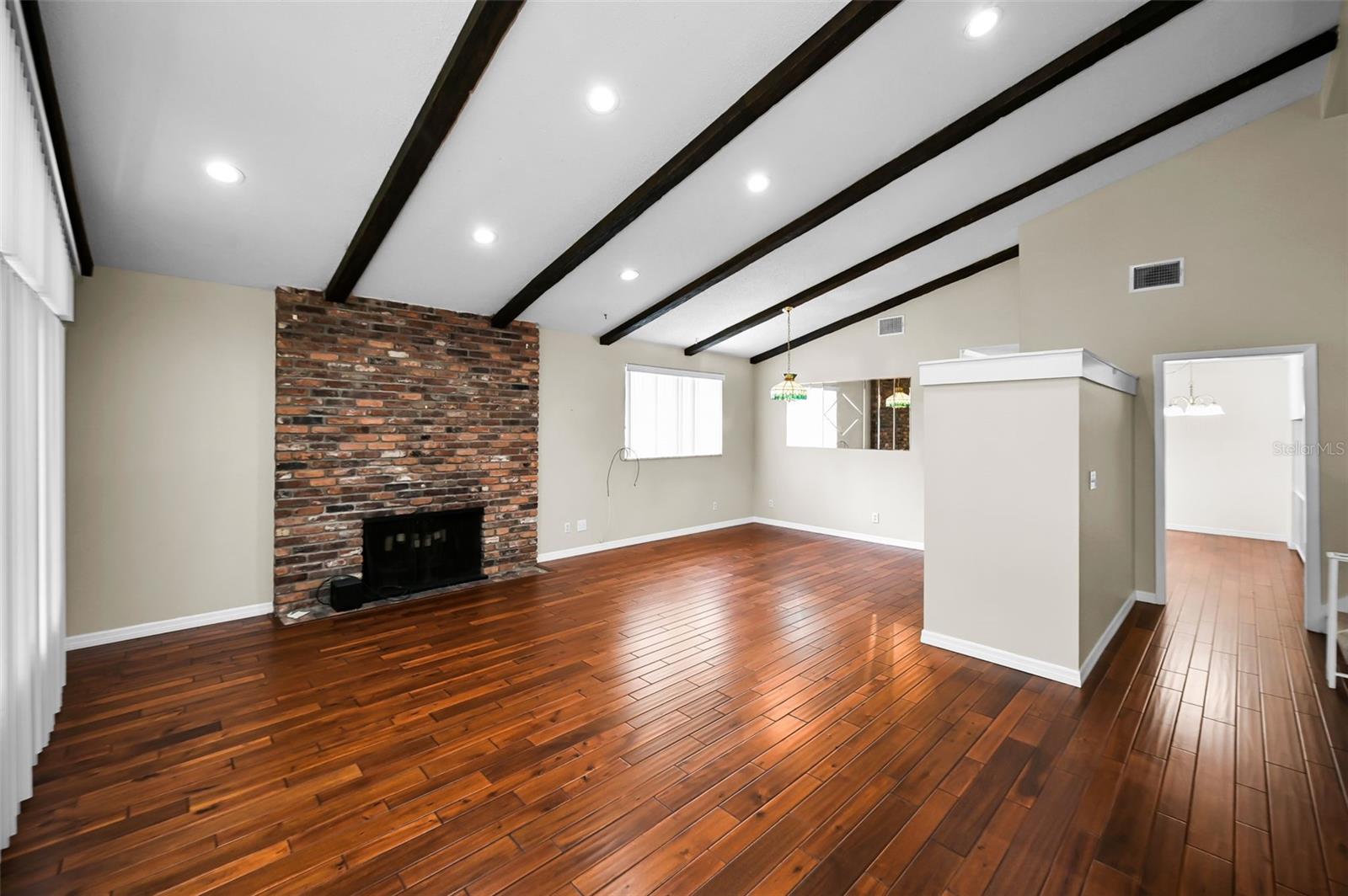 A striking living room featuring a vaulted, beamed ceiling, a commanding fireplace, and rich hardwood floors