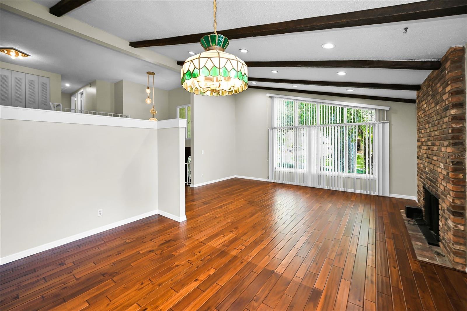 Large living and dining room area with gleaming wood floors and beamed, vaulted ceiling.