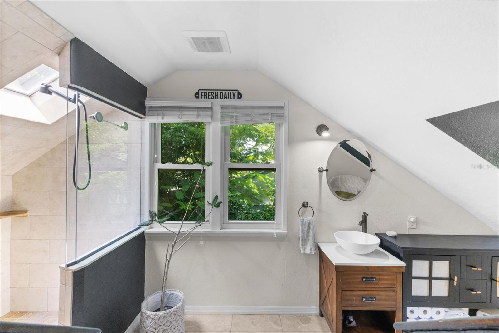 Oversized tiled walk-in shower with skylight, rain-style fixtures, and a bright garden outlook.