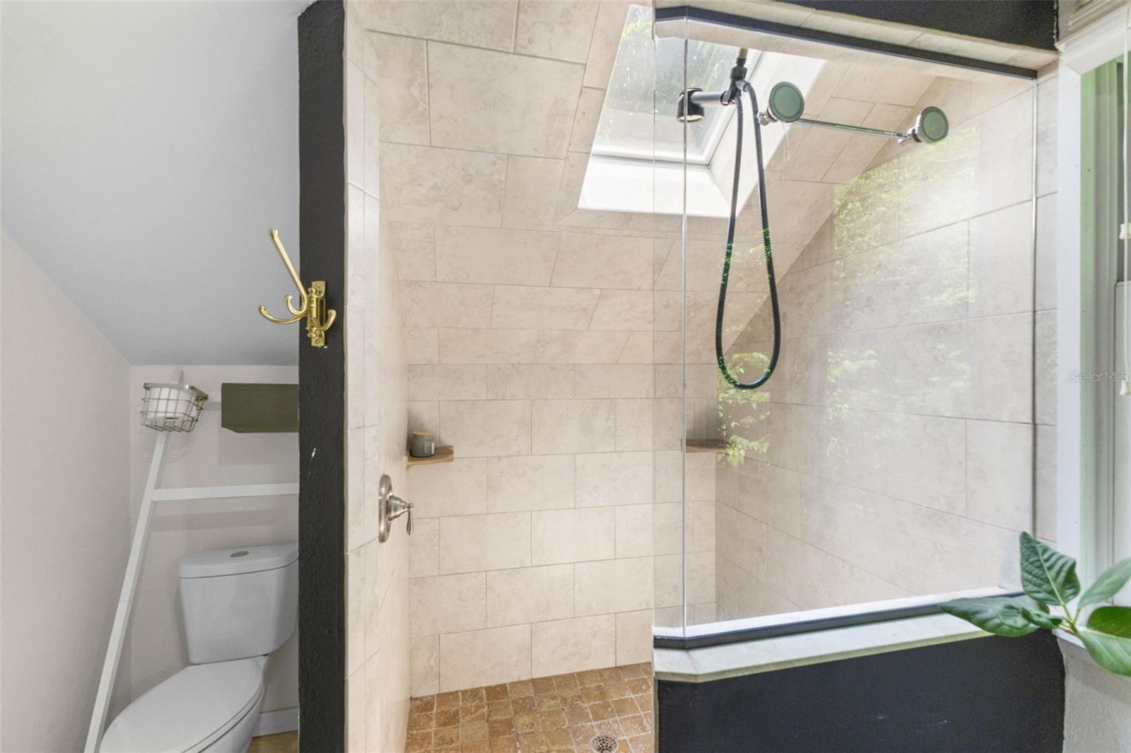 Spa-style upstairs bath featuring a walk-in glass shower, twin wood vanities, and a skylight for natural light.
