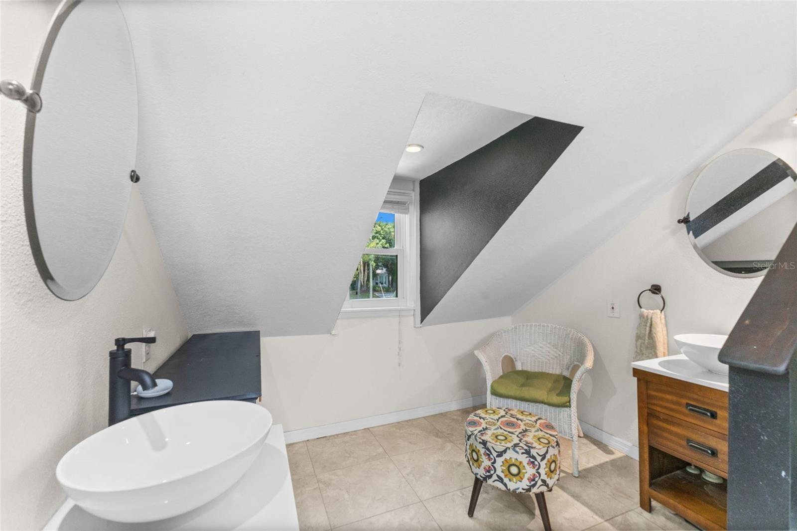 Bright en-suite bath with walk-in tiled shower, skylight, vessel-sink vanity, and a leafy treetop window view.