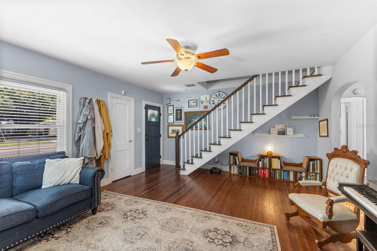 Inviting entry and living space with a striking staircase to the private upstairs suite and cozy built-in reading nook.anchored by warm hardwood floors and classic architectural arches.