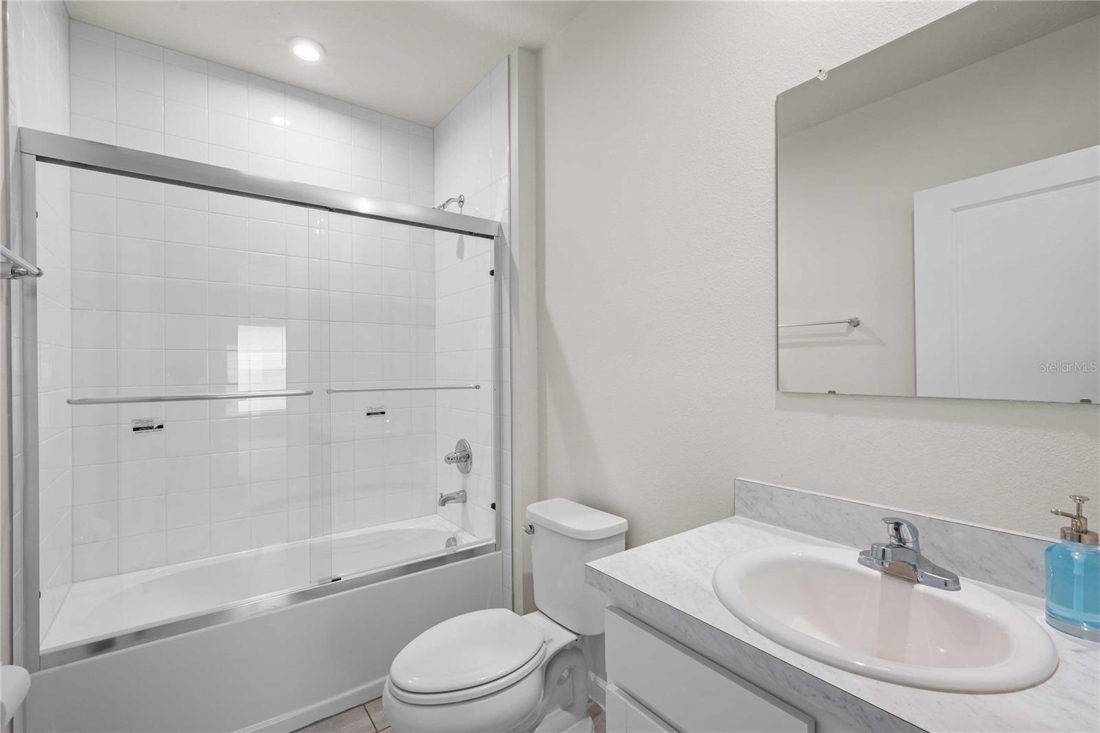 The guest bath has a tub with tile shower surround and a new glass sliding door