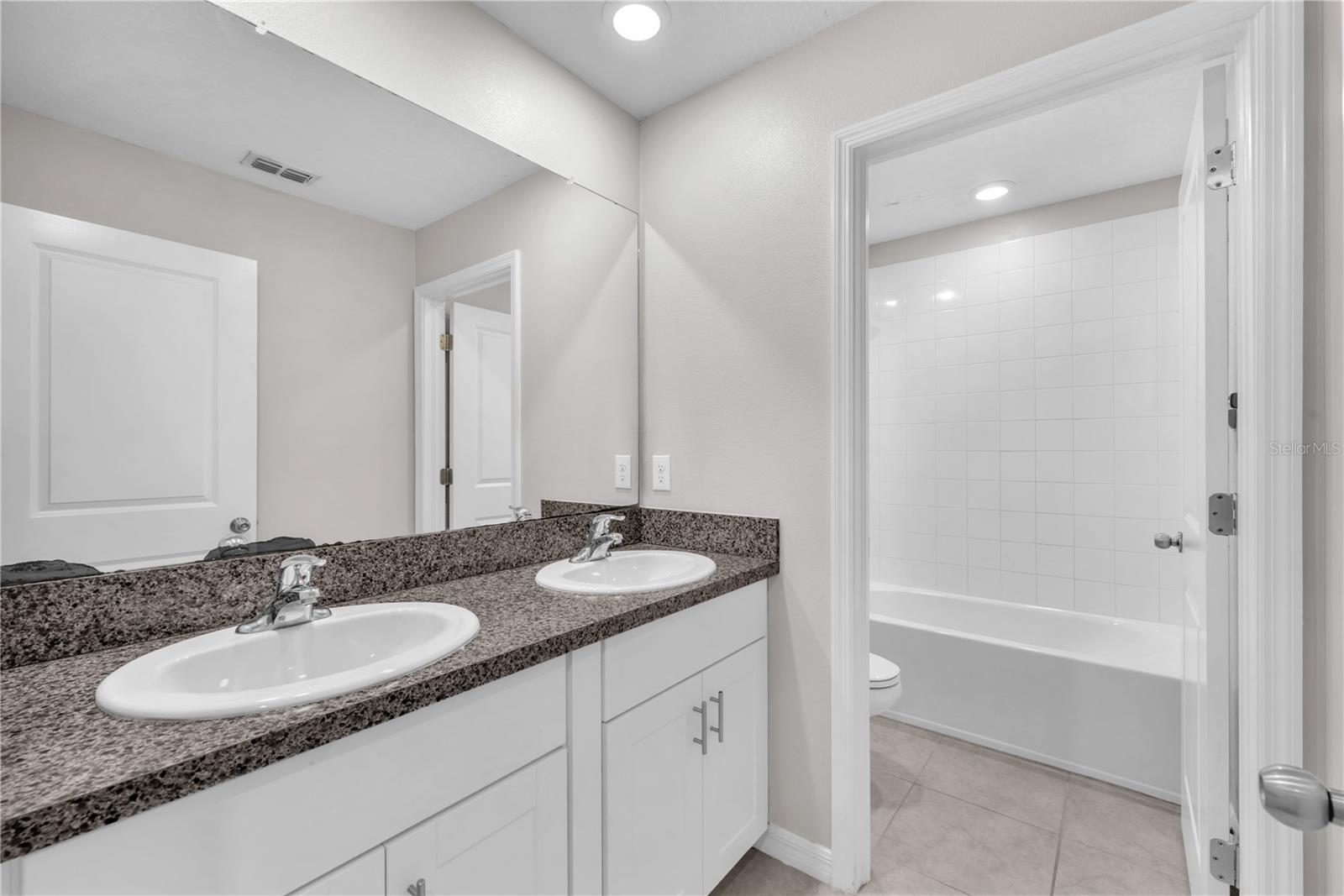 Jack & Jill bathroom with dual sinks and separate room with tub/shower combination and toilet.