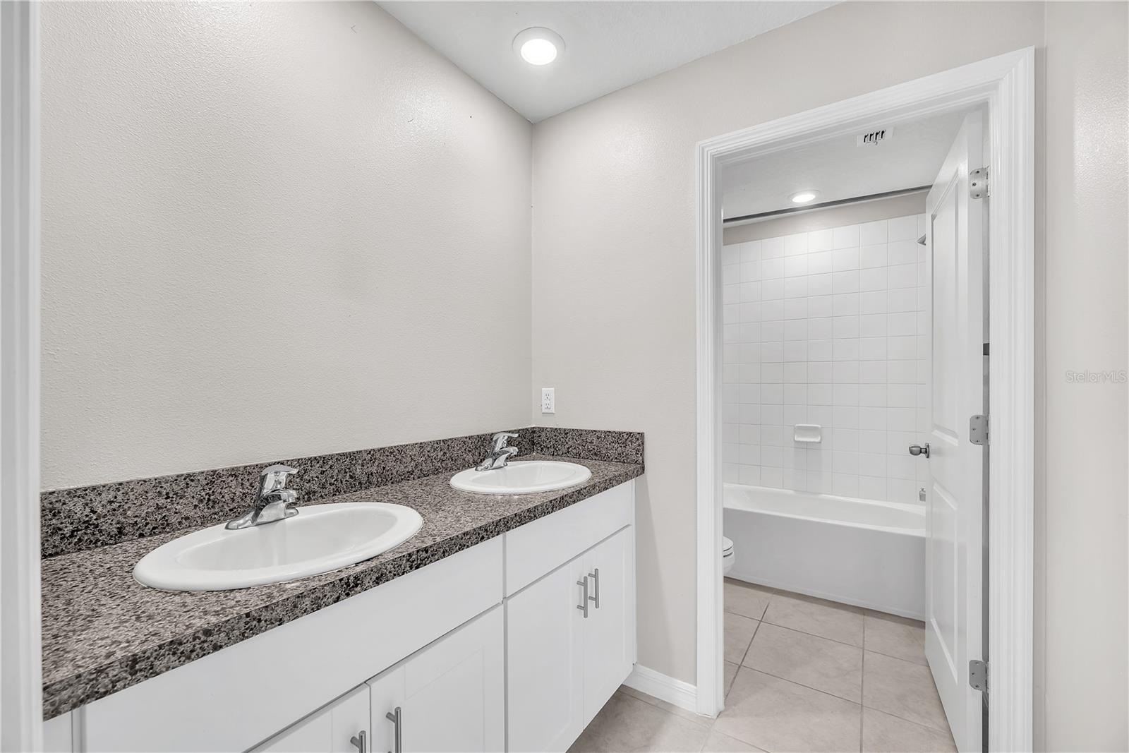 Jack & Jill bathroom with dual sinks and separate room with tub/shower combination and toilet.