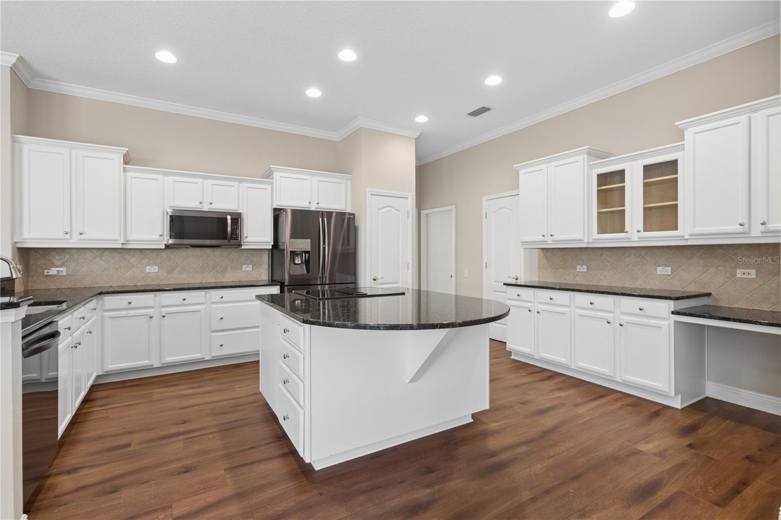 The heart of the home, the open kitchen features generous counter space, abundant cabinetry, a built-in desk, and relaxing views of the pool.