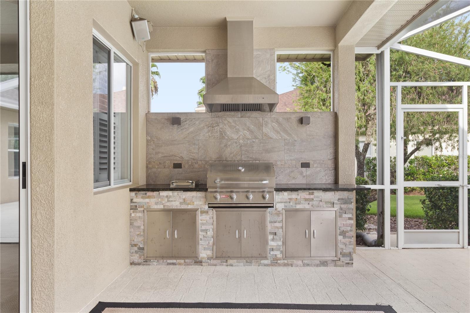 The custom outdoor kitchen features a built-in gas grill, vent hood, and thoughtfully placed lighting that beautifully illuminates the cooking area for effortless day or evening entertaining.