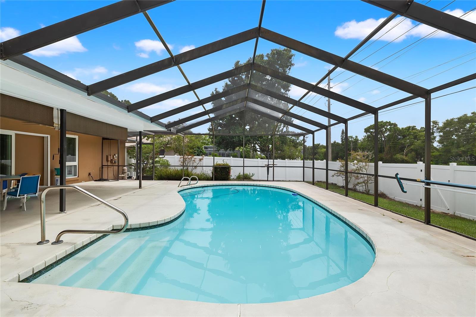An oversized, screen-enclosed pool anchors the backyard, its curved edges and open sun deck offering room to swim, lounge, or entertain. Framed by mature trees and a white privacy fence, it's a private, resort-style escape just steps from the back door.