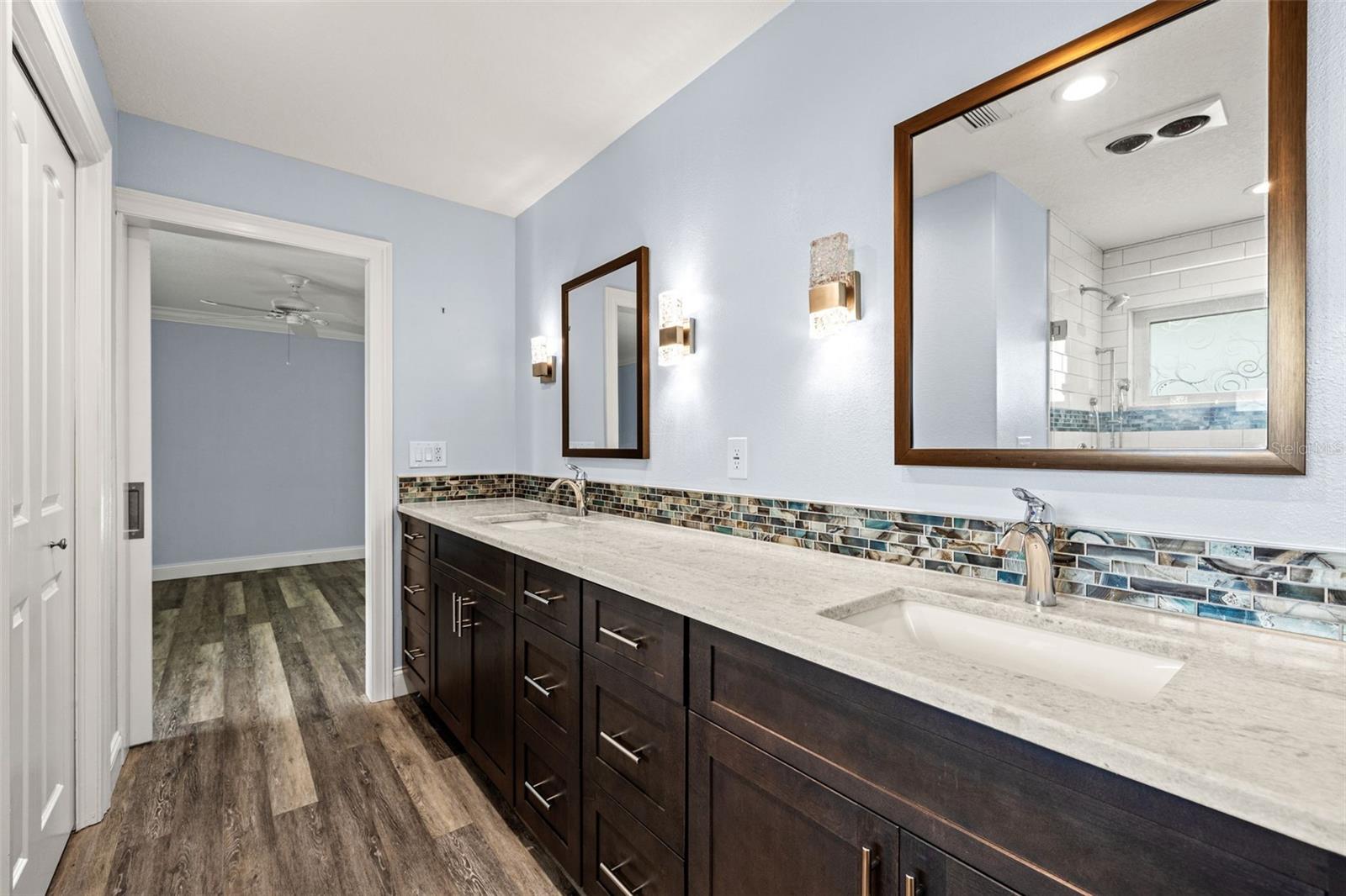 A second view of the primary bath highlights the full length of the dual vanity and the continuity of wood-look flooring throughout.