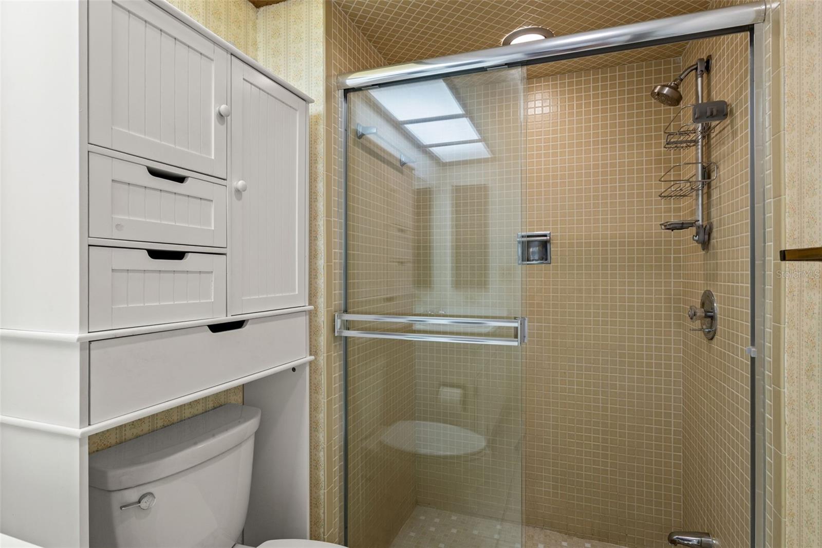 A closer look at the glass-enclosed shower shows the tan tile surround and built-in linen storage, keeping towels and essentials within easy reach.