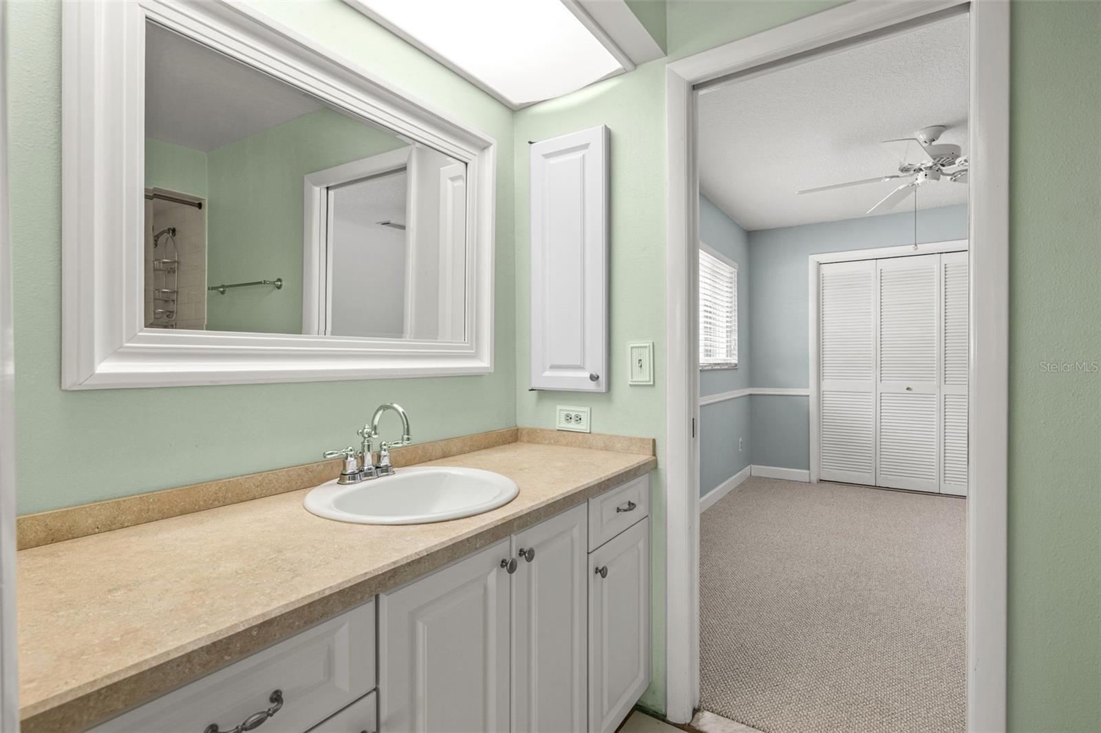 A single vanity with a mirrored medicine cabinet rounds out this shared bathroom, framed by soft green walls and warm countertop tones.